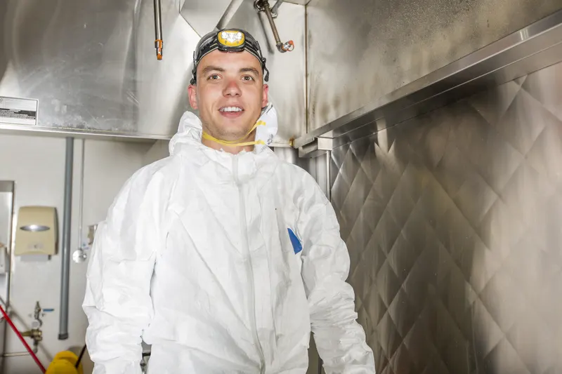 Hood cleaning technician in protective coveralls, goggles and a headlamp standing under a commercial kitchen hood