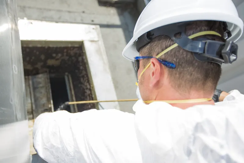 Technician in a white hard hat working at an opened exhaust duct access hatch
